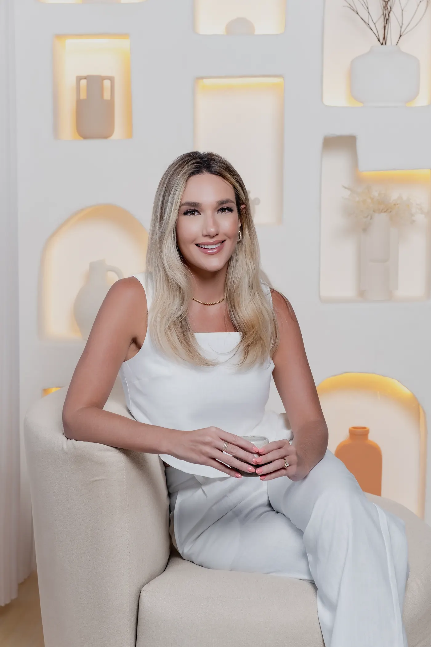 Dra. Vickie White de branco, sentada em uma poltrona clara, diante de nichos iluminados.