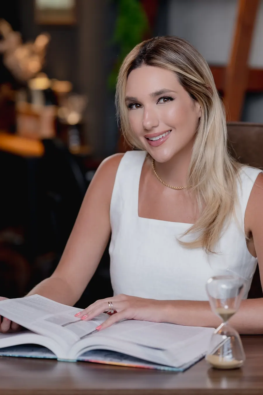 Dra. Vickie White à mesa, com um livro aberto e uma ampulheta.